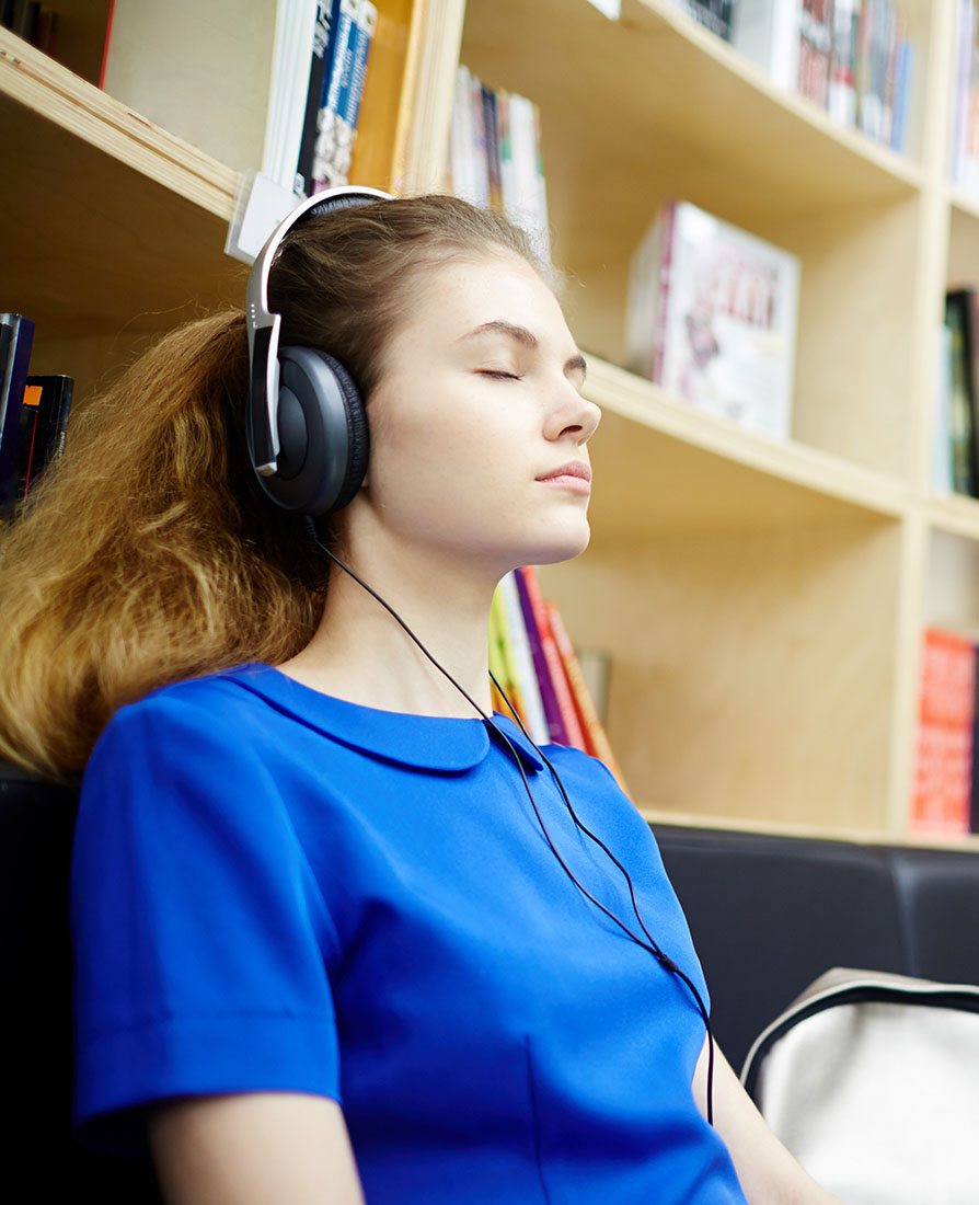 Chica sentada en el suelo de una biblioteca escuchando música con unos cascos