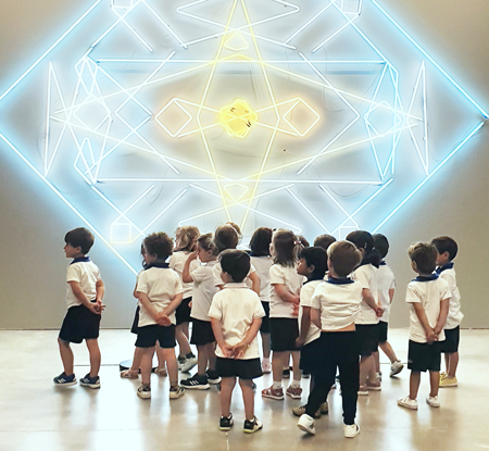 Group of children in a room looking at a neon